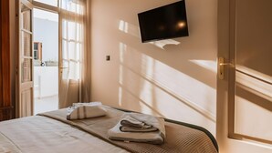 A hotel room with a bed, a flat-screen TV mounted on the wall, and a window with curtains. - Casa Autentica 1933 Apartment with Private Balcony (Kos)