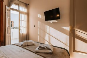 Ein Hotelzimmer mit Bett, einem an der Wand befestigten Flachbildfernseher und einem mit Vorhängen versehenen Fenster.