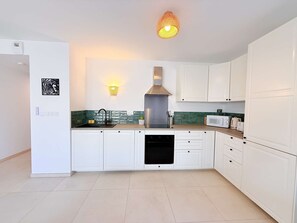 A modern kitchen with white cabinets, a stainless steel range hood, a microwave, and a sink. - Apartment with parking - 5 guests (Le Lavandou)