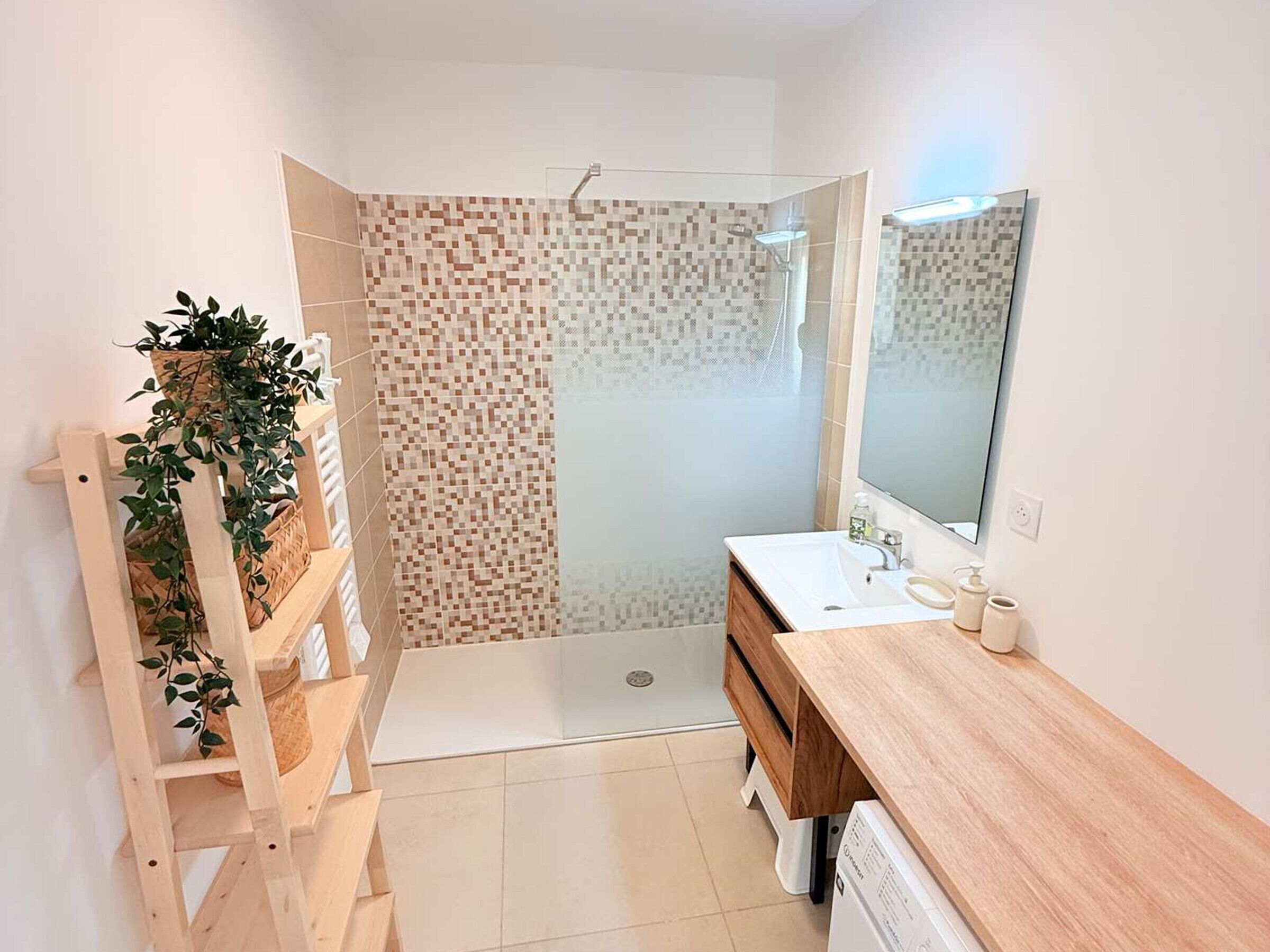Une salle de bain moderne équipée d’une douche, d’un lavabo, d’un miroir et d’une étag ère en bois agrémentée de plantes.