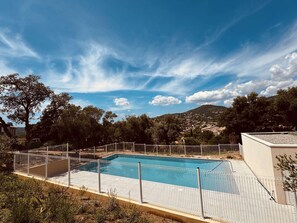 Ein rechteckiger Pool mit weißem Zaun, umgeben von Bäumen und Hügeln im Hintergrund.