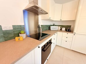 Eine moderne Küche mit eingebautem Herd, Mikrowelle und Wasserkocher. Auf der Arbeitsfläche steht ein Willkommensschild und ein Blumentopf.