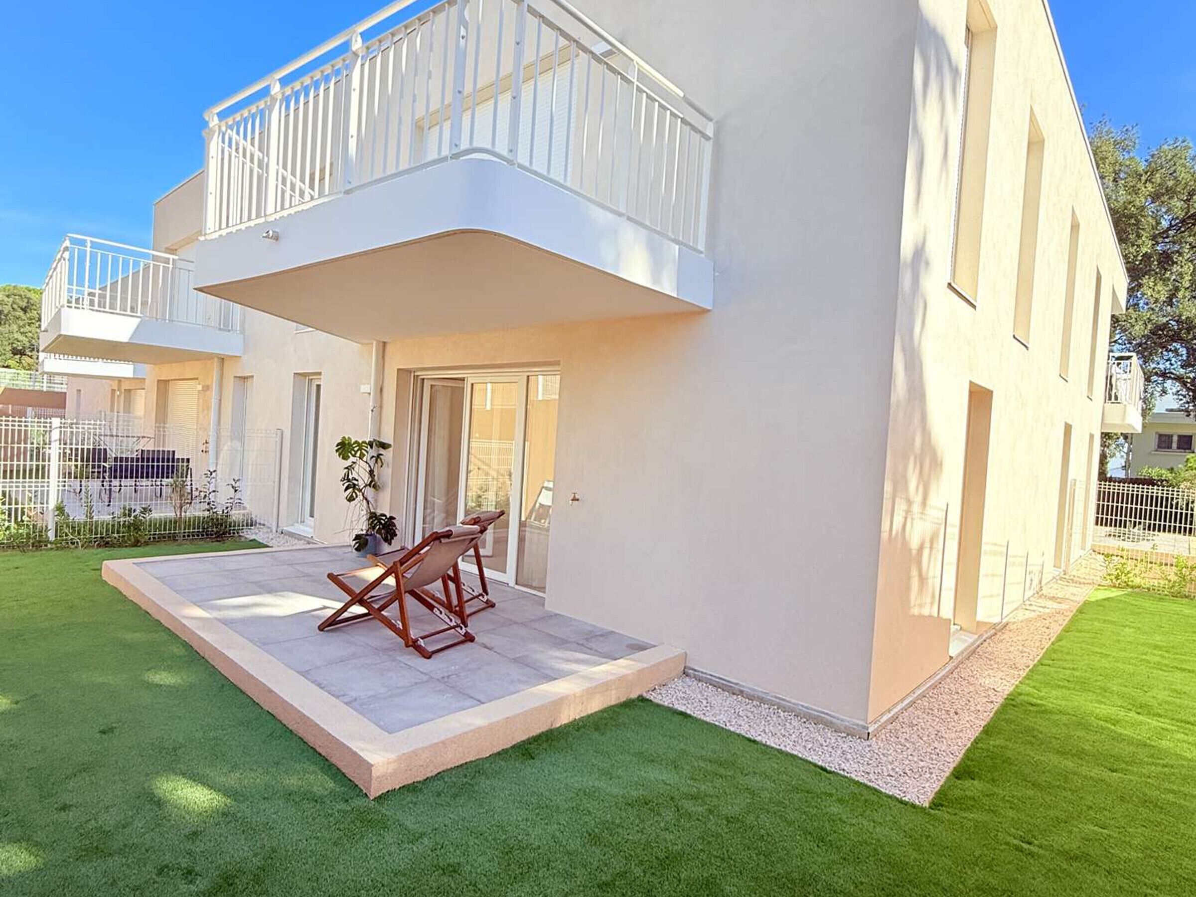 Ein modernes Wohnhaus mit zwei Etagen, einem Balkon, einer kleinen Terrasse mit einem Stuhl und einem gepflegten Rasen.