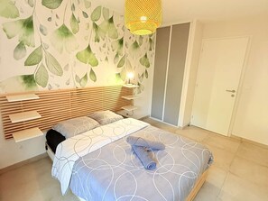 A bedroom with a bed, a nightstand, a wall-mounted lamp, and a wardrobe. - Apartment, air conditioning, parking - 4 guests (Le Lavandou)