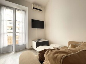 Ein Hotelzimmer mit Bett, Wandfernseher, Nachttisch und einem fenster mit Vorhängen.
