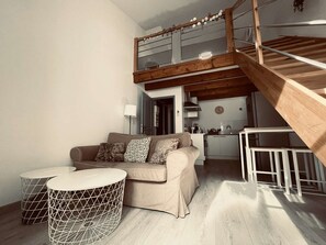 Ein Wohnbereich im Loft-Stil mit einer Holztreppe, einer Couch mit gemusterten Kissen und einer Küche im Hintergrund.