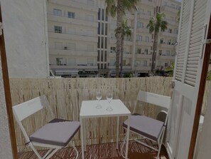 Ein Balkon mit Tisch und zwei Stühlen, mit Blick auf ein Gebäude mit mehreren Balkonen und Palmen.