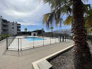 A rooftop pool area with a clear sky, surrounded by buildings and palm trees. - T2 Apartment with pool and AC - spacious lodging (Le Lavandou)