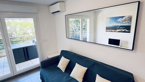 Un salon moderne avec un canapé vert foncé, un grand miroir et une vue sur la verdure à l’extérieur.