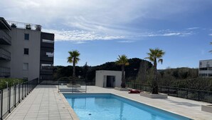 Une piscine avec une terrasse carrelée, entourée d’une petite clôture, et des palmiers en arrière-plan.