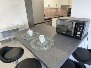 A modern kitchen with a microwave, two white mugs, and a bar stool. - T2 Apartment with pool and AC - spacious lodging (Le Lavandou)