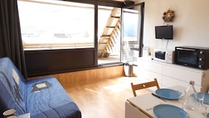 En kompakt opholdsstue med sofa, spisebord til to, mikroovn og fjernsyn.