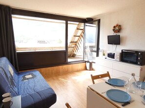 Ein kompakter Wohnraum mit Sofa, Esstisch für zwei Personen, Mikrowelle und Fernseher.