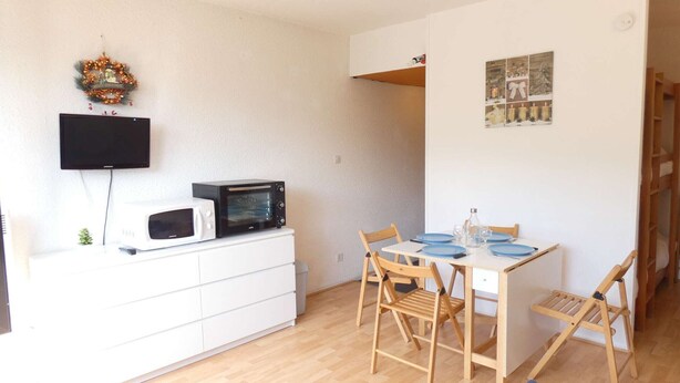 En kompakt opholdsstue med spiseplads, et hvidt skab med mikroovn, et fladskærms-tv og en lille plante.