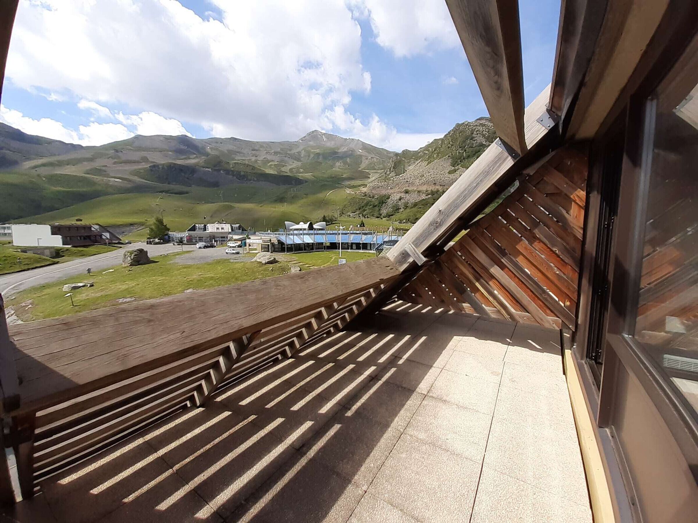 A view from a balcony with a wooden railing overlooking a parking area and buildings in a mountainous area.