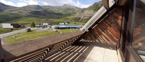 A view from a balcony with a wooden railing overlooking a parking area and buildings in a mountainous area.