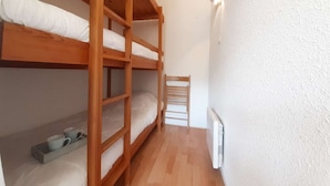 Et lille, aflangt rum med to trækøjesenge, en hvid radiator og en træstol.