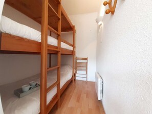 Ein kleiner, schmales Zimmer mit zwei Holzbettgestellen, einem weißen Heizkörper und einem Holzstuhl.