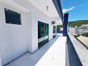 Un balcón con una pared exterior blanca, una puerta de cristal y vistas a una colina verde.