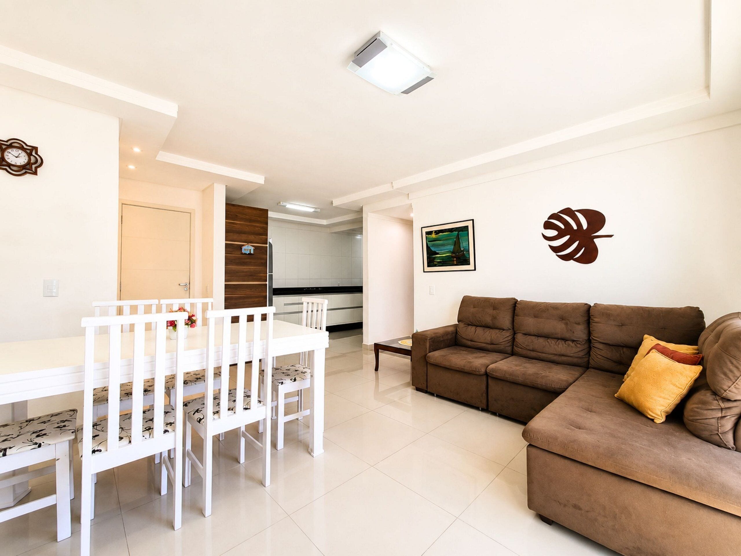 Uma sala de estar moderna com um sofá marrom e uma mesa de jantar com cadeiras brancas.