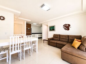 A modern living room with a brown sofa and a dining table with white chairs. - Mont Blanc by LikeHome (Bombinhas)