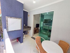 A room with a kitchen area, a dining table with chairs, and a sliding glass door leading to a balcony. - Mont Blanc by LikeHome (Bombinhas)