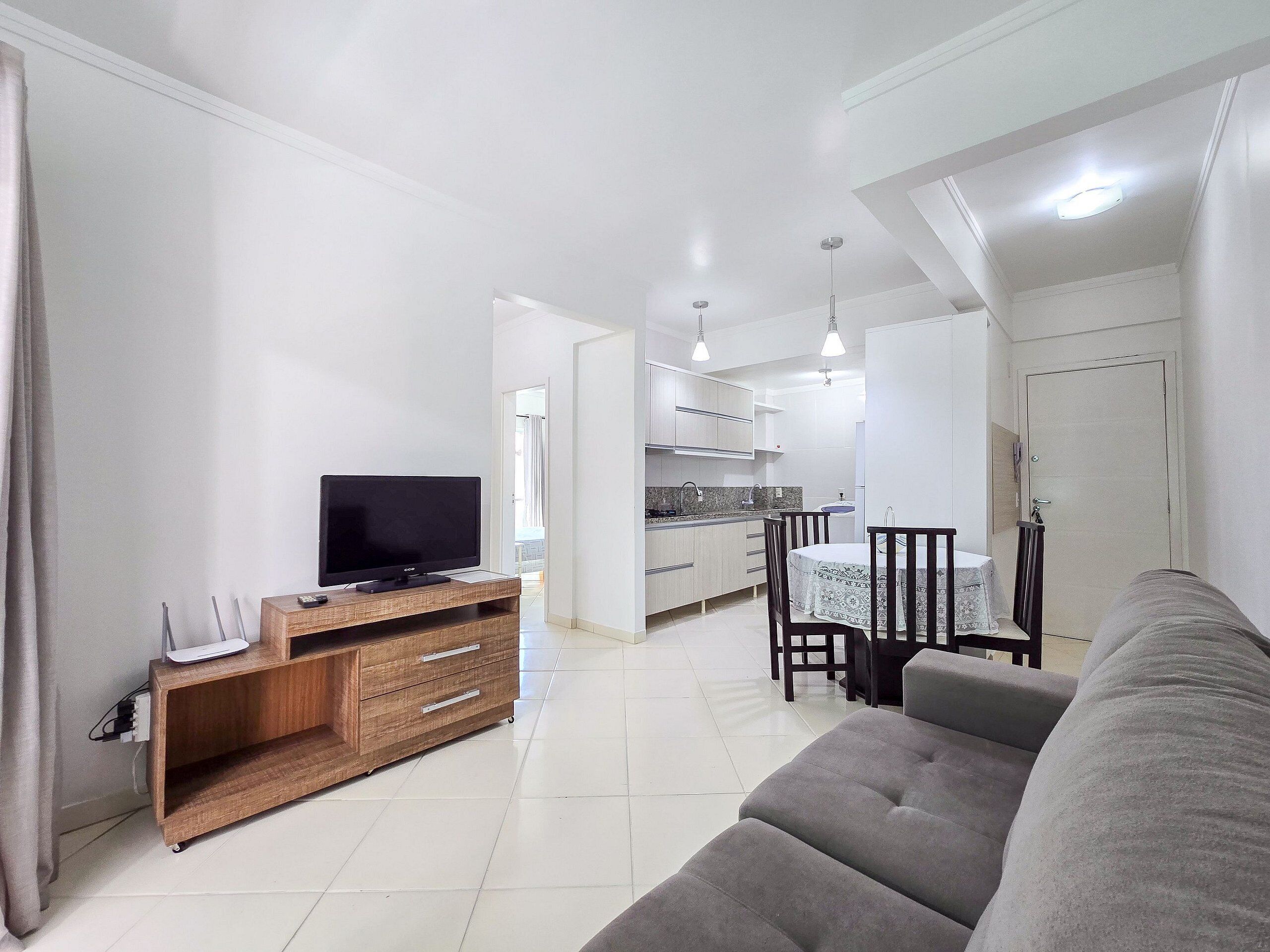 Una sala de estar con un sofá, un televisor sobre un mueble de madera y un comedor con una mesa y sillas.