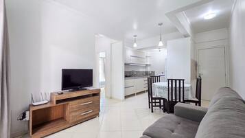 Una sala de estar con un sofá, un televisor sobre un mueble de madera y un comedor con una mesa y sillas.