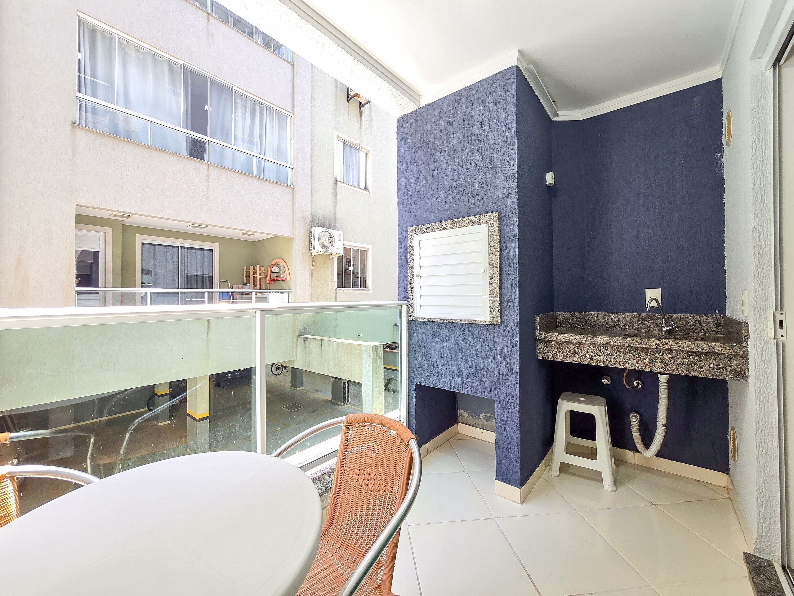 Un balcón con barandilla de vidrio, una mesa y una silla de mimbre.