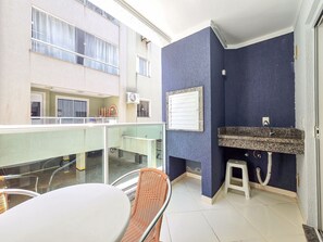 Un balcón con barandilla de vidrio, una mesa y una silla de mimbre.