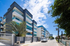 Um edifício residencial moderno, com várias andares, varandas, portão fechado e céu claro.