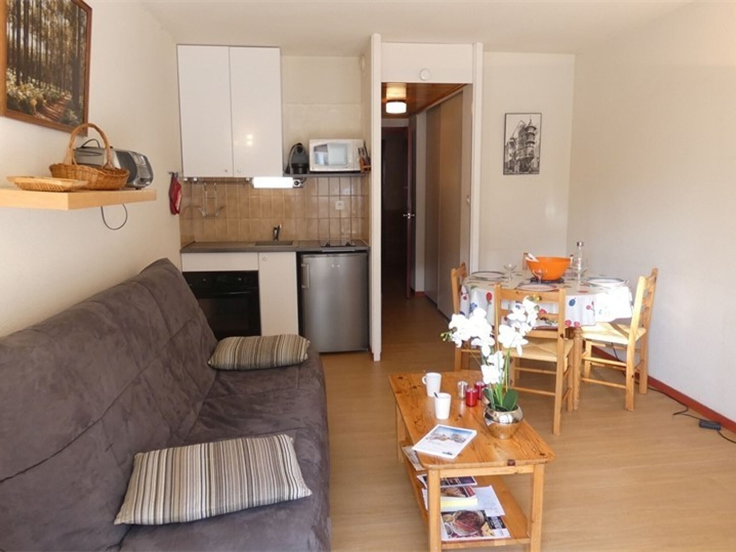 A compact living space with a kitchenette, a dining area, and a sofa with cushions.