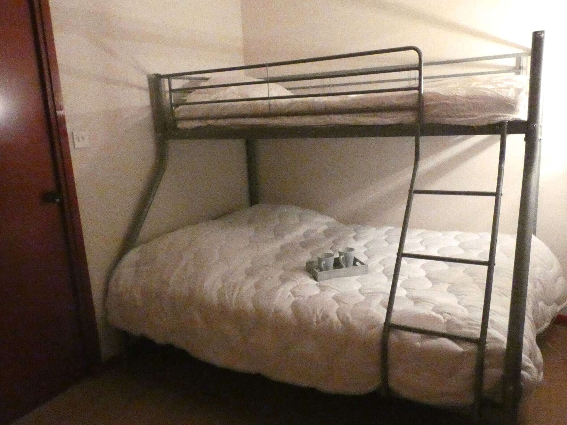 Una cama litera con escalera, una bandeja con tazas y una puerta a la izquierda.