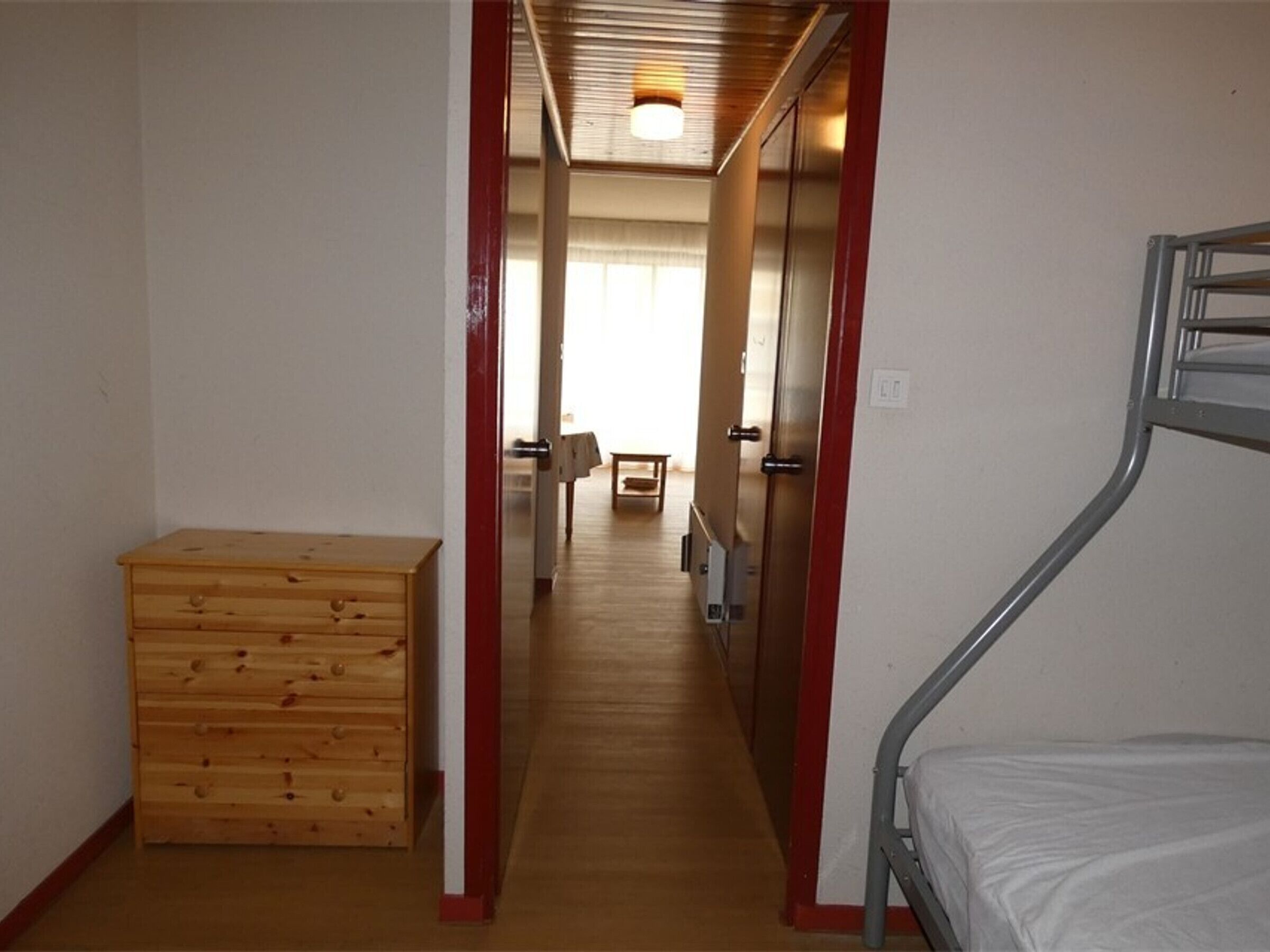 Een smalle gang met een stapelbed aan de rechterkant, een houten dressoir aan de linkerkant en een deur naar een andere kamer.