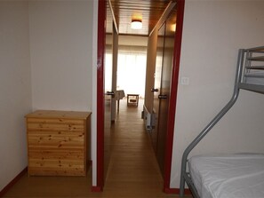 Ein schmaler Flur mit einem Etagenbett rechts, einer Holzkommode links und einer Tür zu einem weiteren Raum.