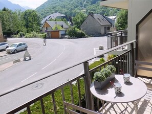 Ein Balkon mit Tisch und Stühlen, der auf eine Straße mit Zebrastreifen und parkenden Autos blickt.