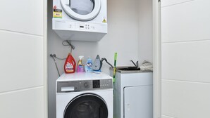 A laundry area with a washing machine, a dryer, and various cleaning supplies. - The Archibald Skyline 25th Floor in Gosford (Gosford)