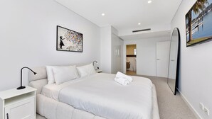 A modern hotel room with a large bed, a bedside table, a lamp, a painting, and a view of a body of water through a window. - The Archibald Skyline 25th Floor in Gosford (Gosford)
