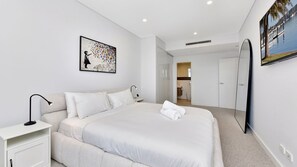 A modern hotel room with a large bed, a bedside table, a lamp, a painting, and a view of a body of water through a window. - The Archibald Skyline 25th Floor in Gosford (Gosford)