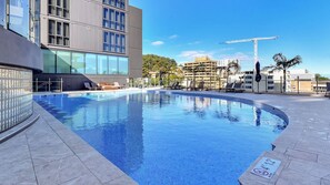 A swimming pool with lounge chairs, a modern building with large windows, and a construction crane in the background.