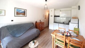 Um espaço compacto com sofá, mesa de jantar com cadeiras, cozinha e uma pequena mesinha lateral.