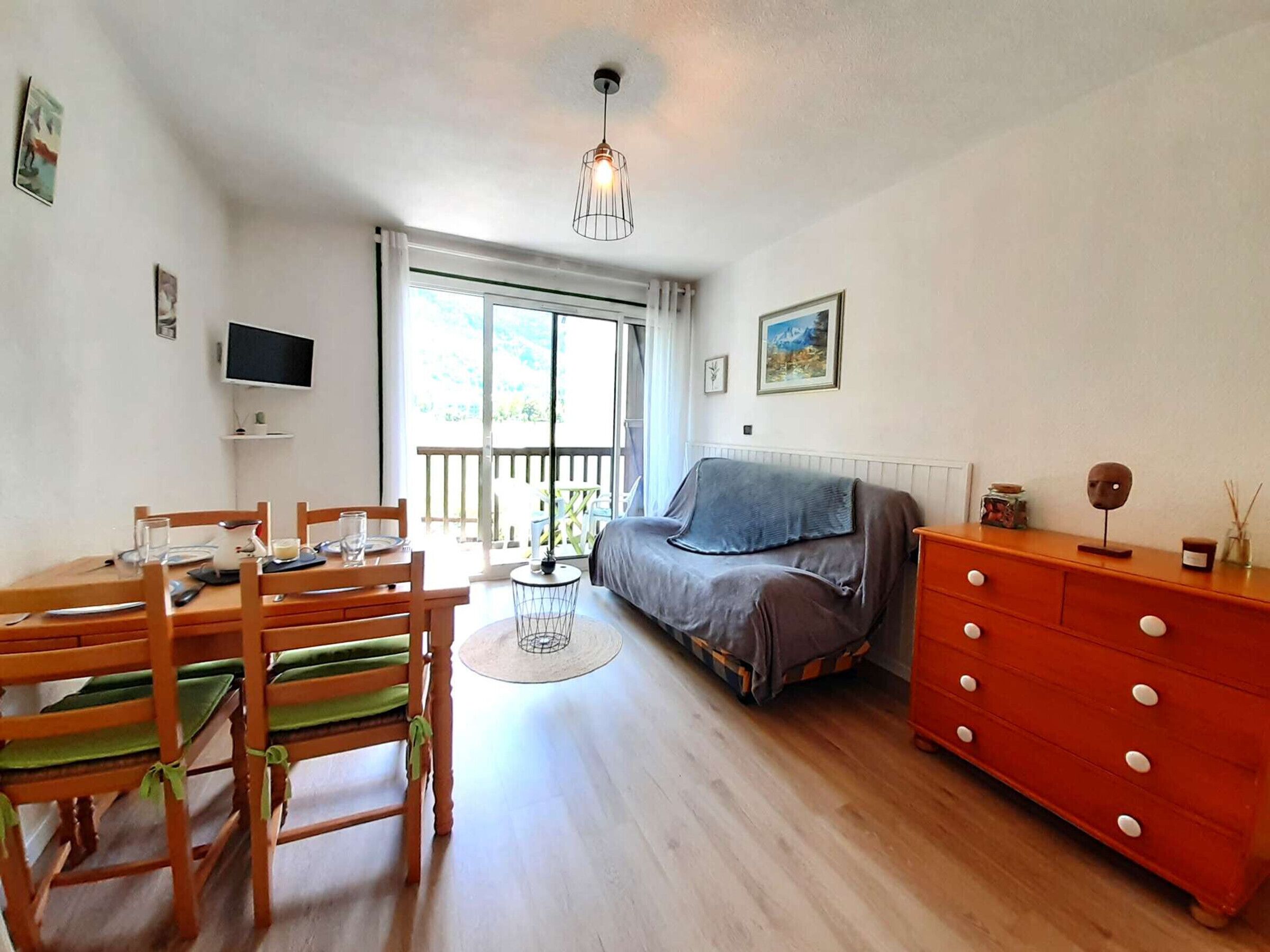 Een kamer met een eettafel, stoelen, een bank, een televisie en een raam met uitzicht.