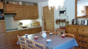 Une cuisine avec des meubles de rangement en bois, une table à manger recouverte d’une nappe à pois et un luminaire suspendu.
