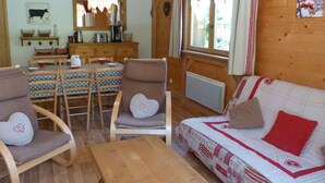 Une pièce chaleureuse avec un plancher en bois, un canapé recouvert d’un tissu à motifs, une table à manger avec des chaises et un coin cuisine agrémenté d’un luminaire suspendu.