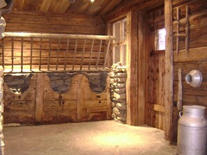 Ein rustikales Holzhaus im Inneren mit einer Steinwand, einer Holztür und einem Metallbehälter.