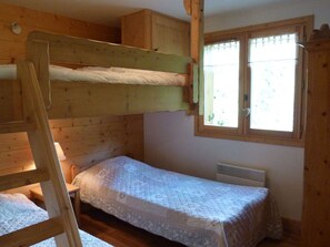A bunk bed room with a window, a heater, and a wooden ladder.