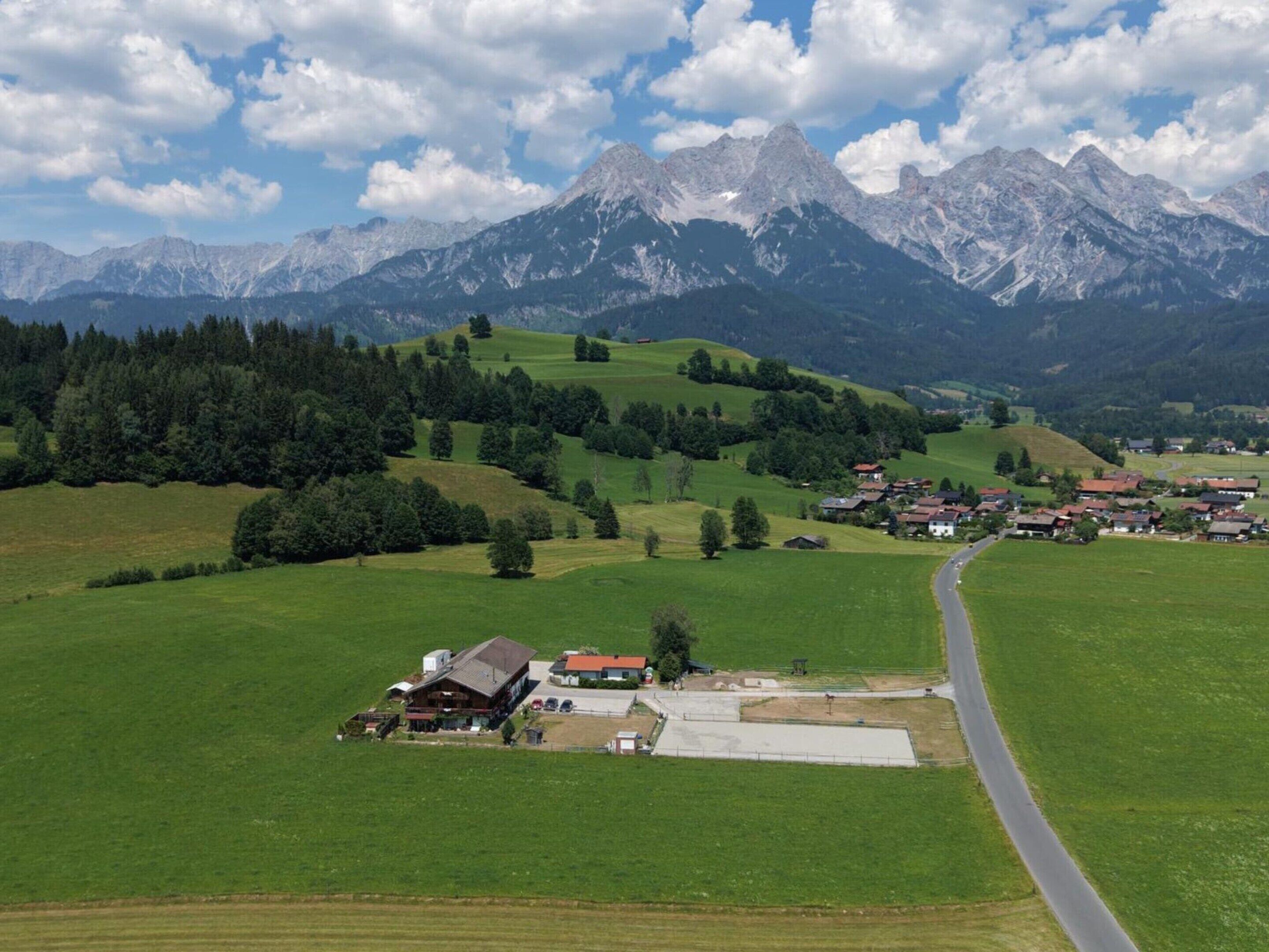 A rural landscape with a road, a large building, and a mountain range in the background.