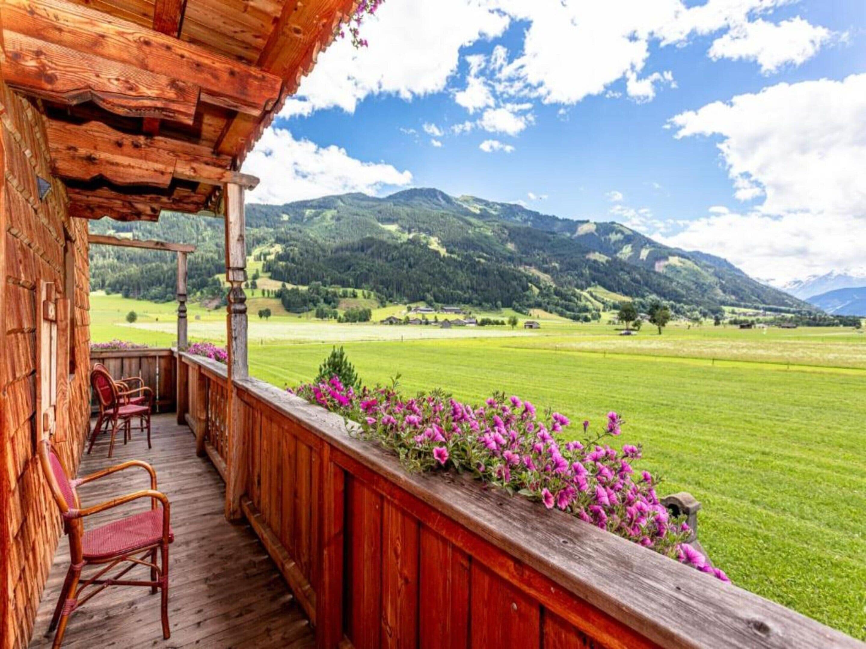 A wooden balcony with a view of a green field and mountains.
