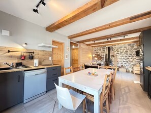 A modern kitchen with a central island, wooden beams, stone walls, and a dining area with a white table and chairs. - Charming house, parking, city center - 8 guests (Mont-Dore)