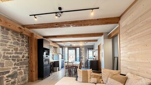 A modern living room with a sectional sofa, a dining area, and a kitchen with stone walls. - Charming house, parking, city center - 8 guests (Mont-Dore)